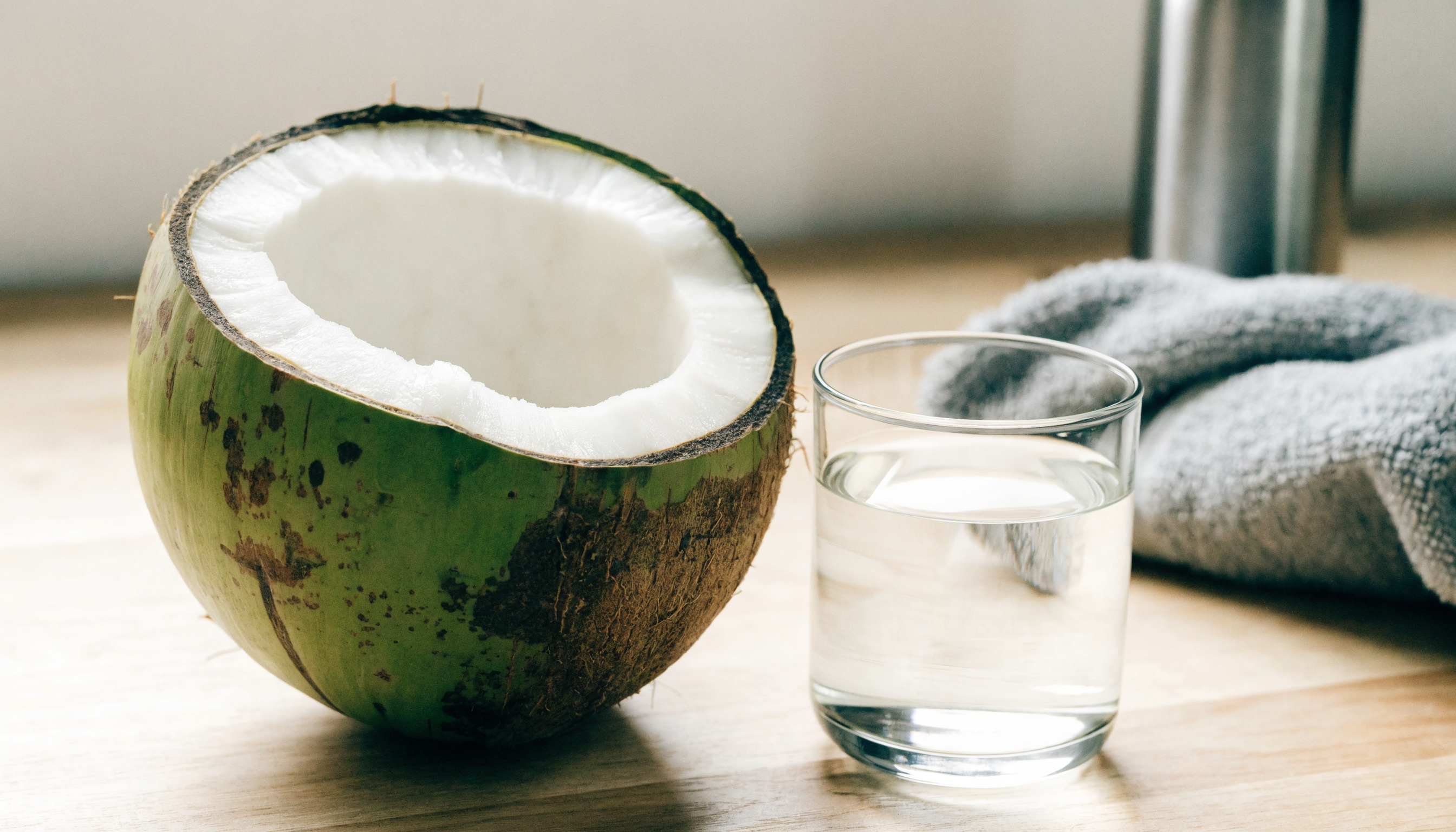 Noix de coco verte ouverte et verre d'eau de coco posés sur une surface en bois clair