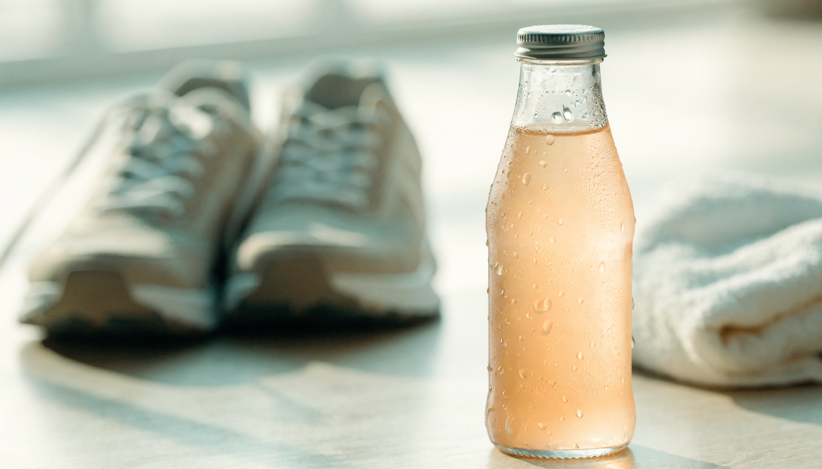 Bouteille de boisson d'hydratation fraîche posée sur du bois clair avec des chaussures de course en arrière plan